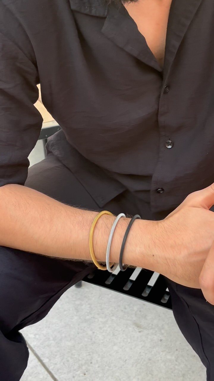 Three thin gold, silver, and black bracelets worn on a man's wrist.