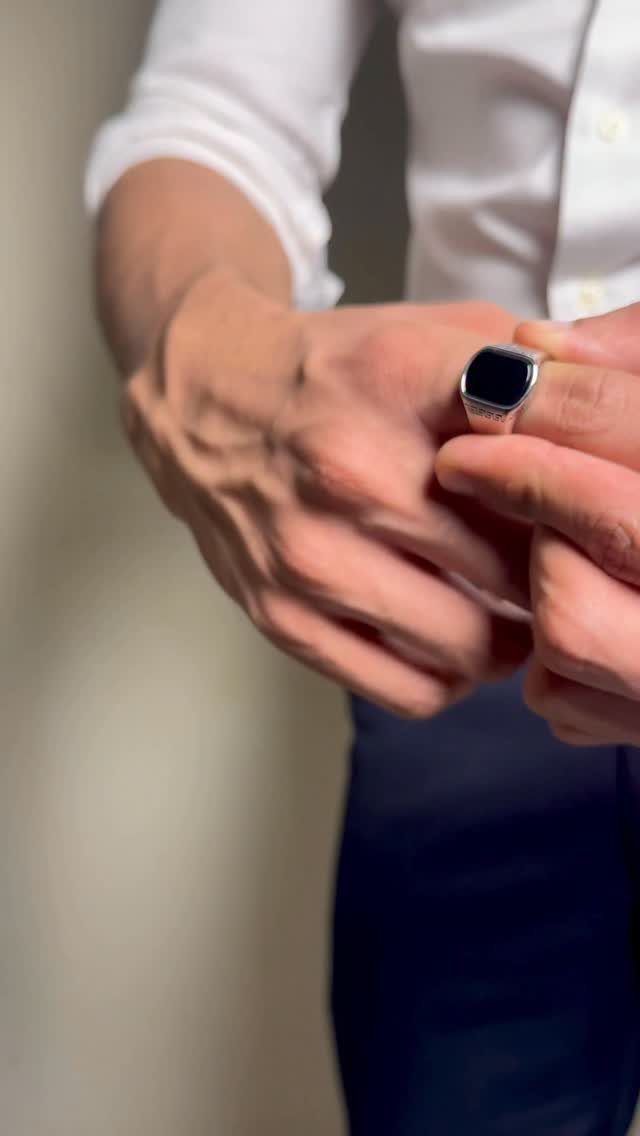 Man's hand wearing a bold square silver ring with a black gemstone center.