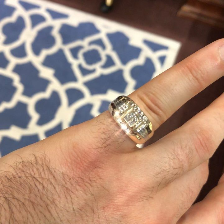 Gold diamond ring worn on a man's finger against a patterned rug background