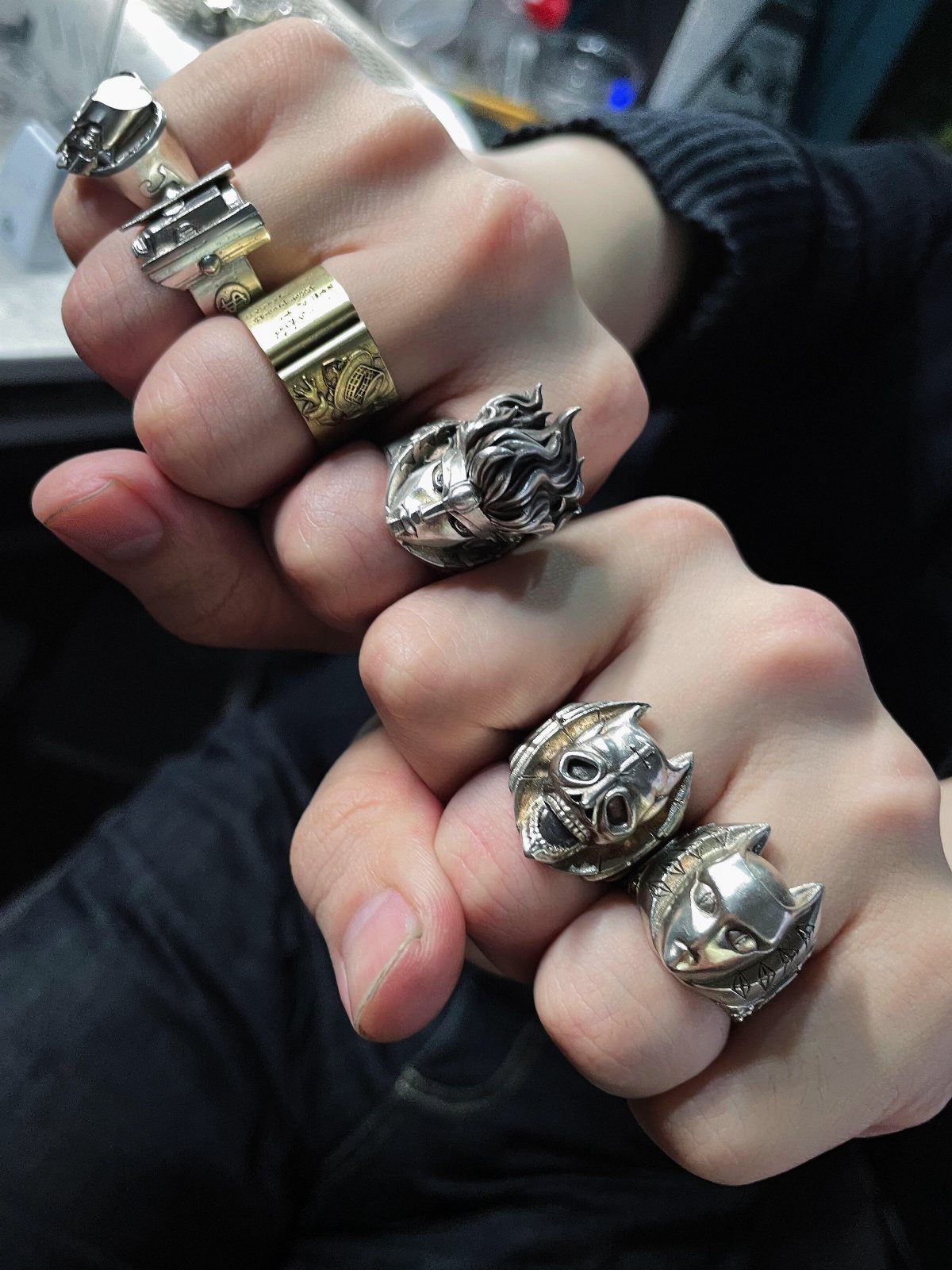 Multiple chunky silver and gold rings layered on a person's fingers.