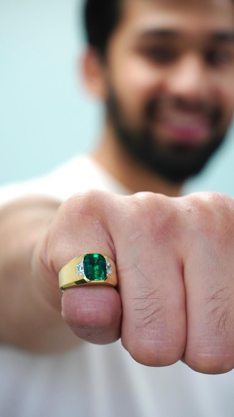 Gold ring with a green emerald worn on a man's pinky finger.
