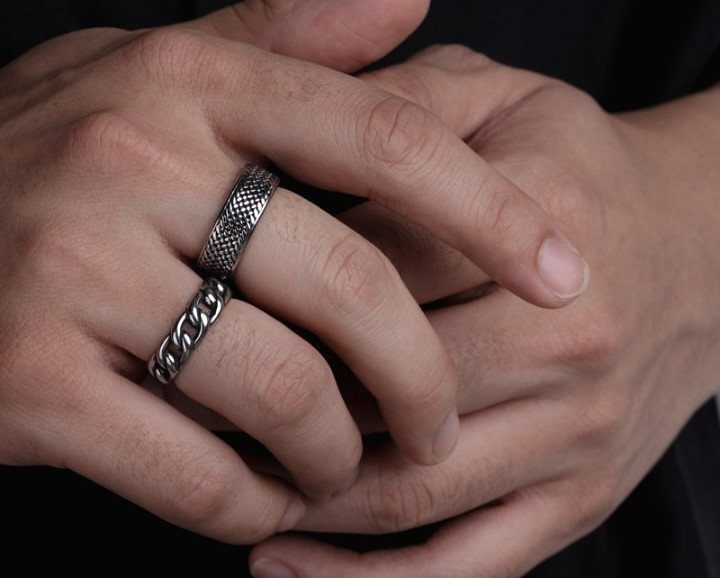 Two silver rings, one textured and one chain-link, worn on a man's finger.