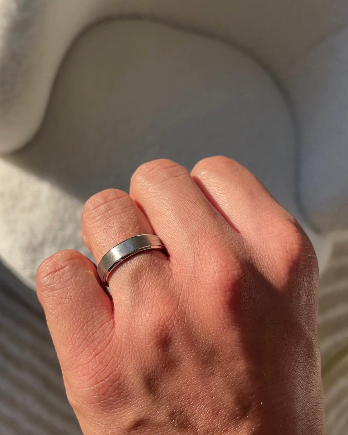Silver-colored metal ring band worn on a person's ring finger against white fabric