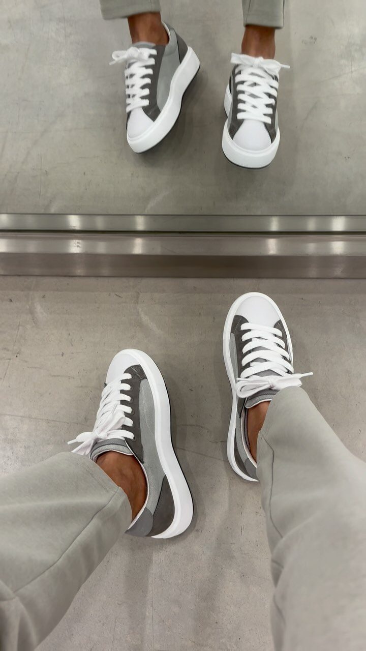 Grey and white sneakers with white laces worn with light grey trousers.