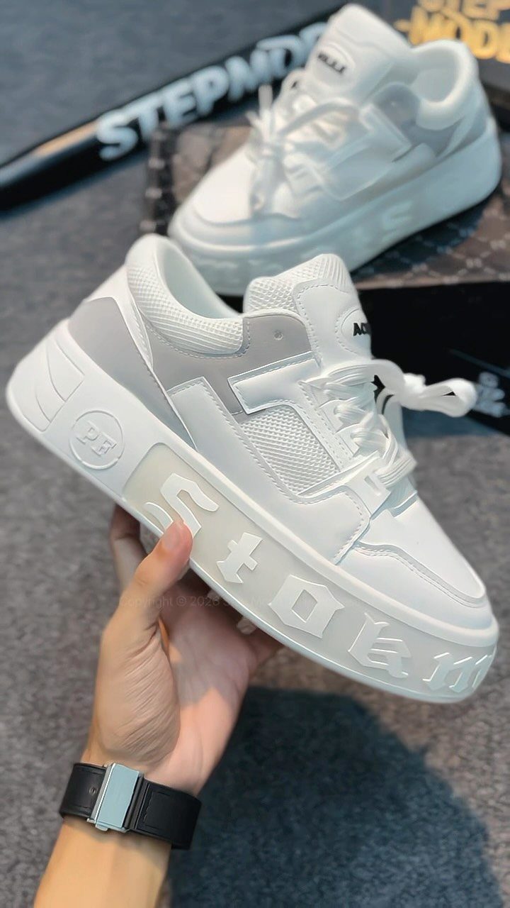 White chunky sneakers with thick embossed soles held by a person's hand.