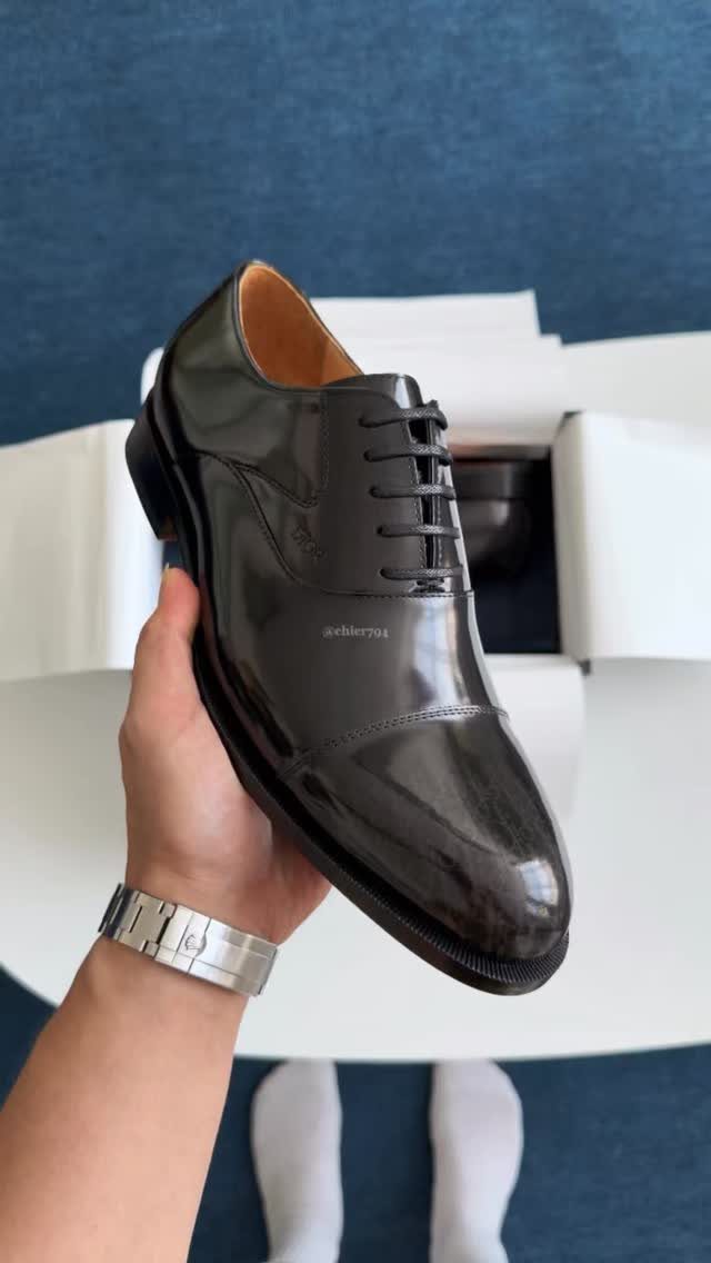 Polished black leather dress shoe held by a hand over a white box.
