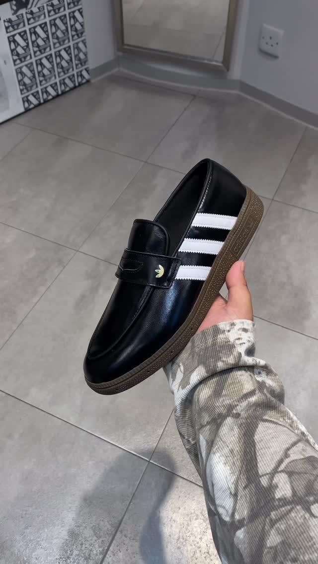 Black leather sneaker loafer with white stripes and brown sole held by hand.