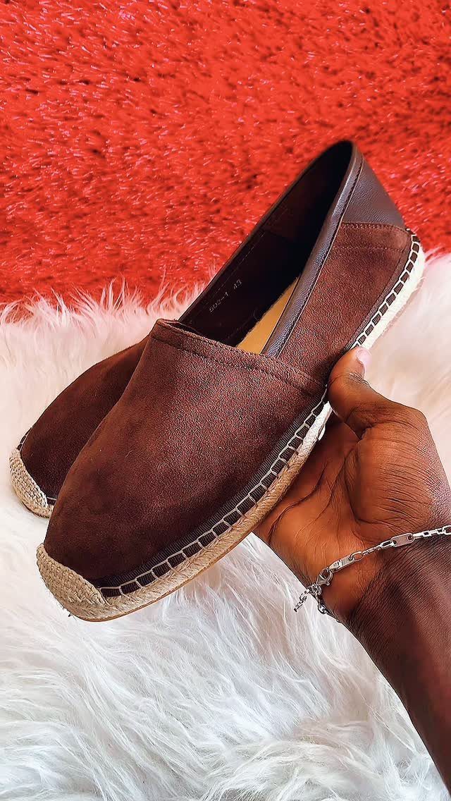 Brown suede espadrilles with jute soles held by a hand over white fur.