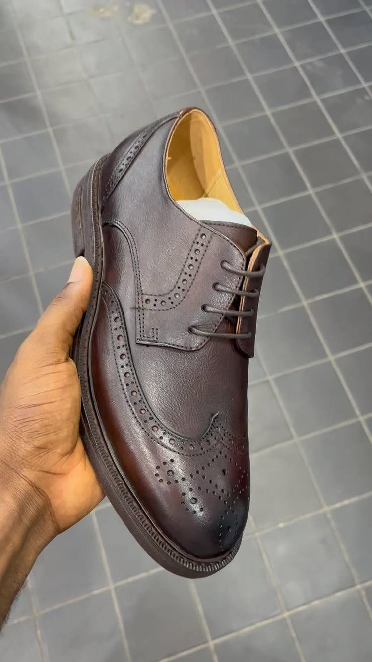Dark brown leather brogue shoe with decorative perforations held by a hand.