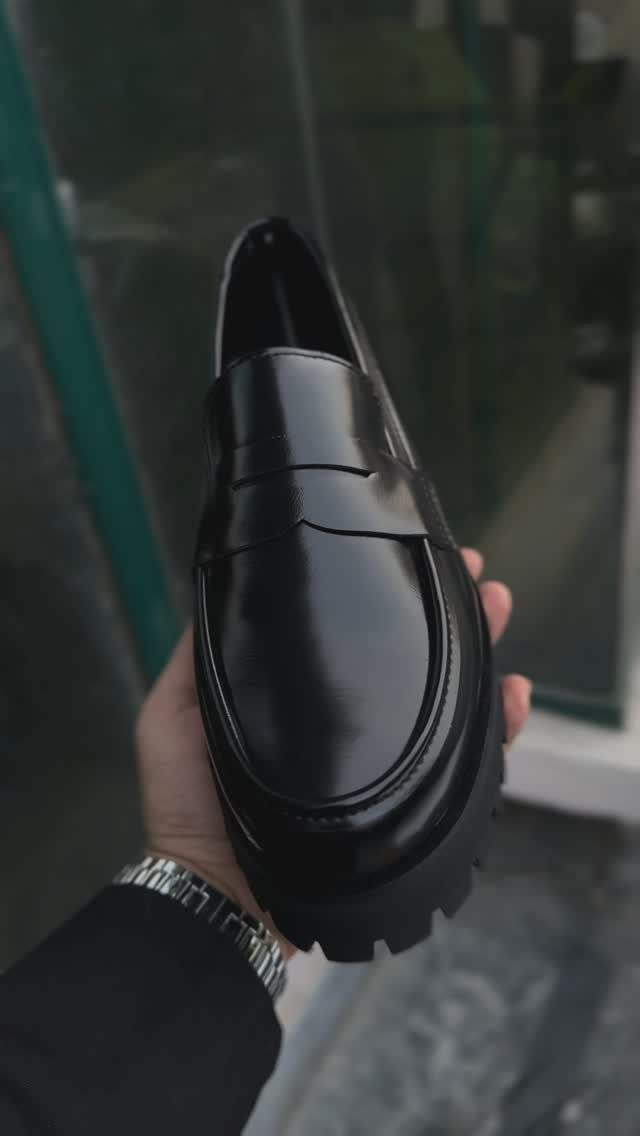 Black leather loafer with a chunky sole held by a person's hand.