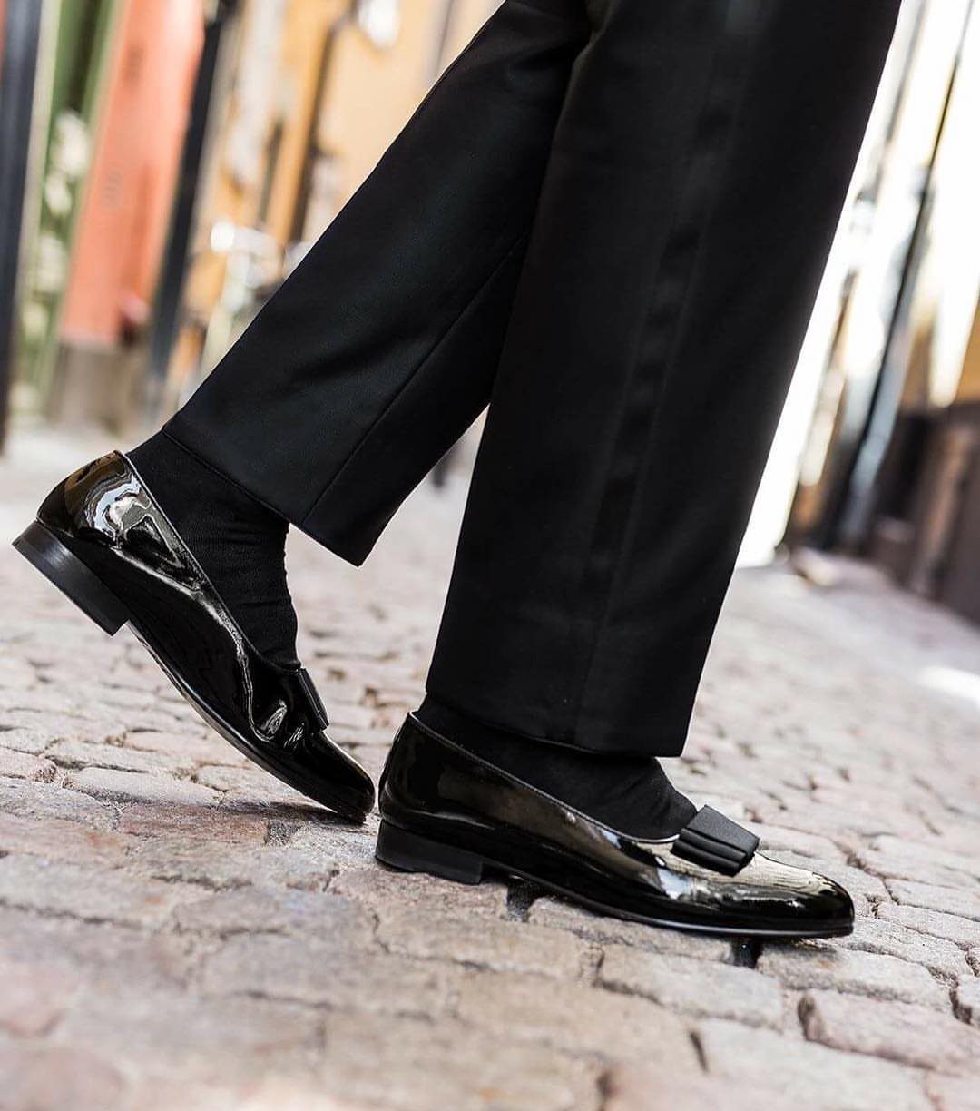 Black patent leather opera pumps with bows worn with black trousers on cobblestones