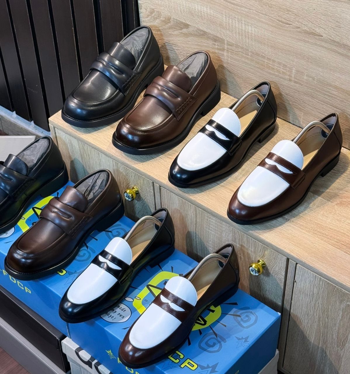 Leather penny loafers in black and brown displayed on wooden store shelves.