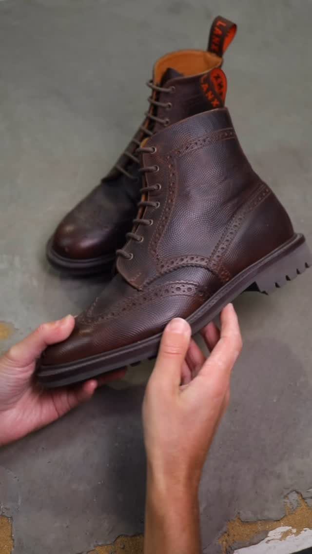 Dark brown leather brogue boots with decorative perforations held by two hands.