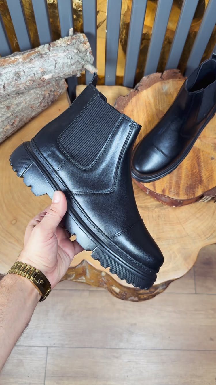 Black leather Chelsea boots with chunky soles displayed on wooden surfaces.