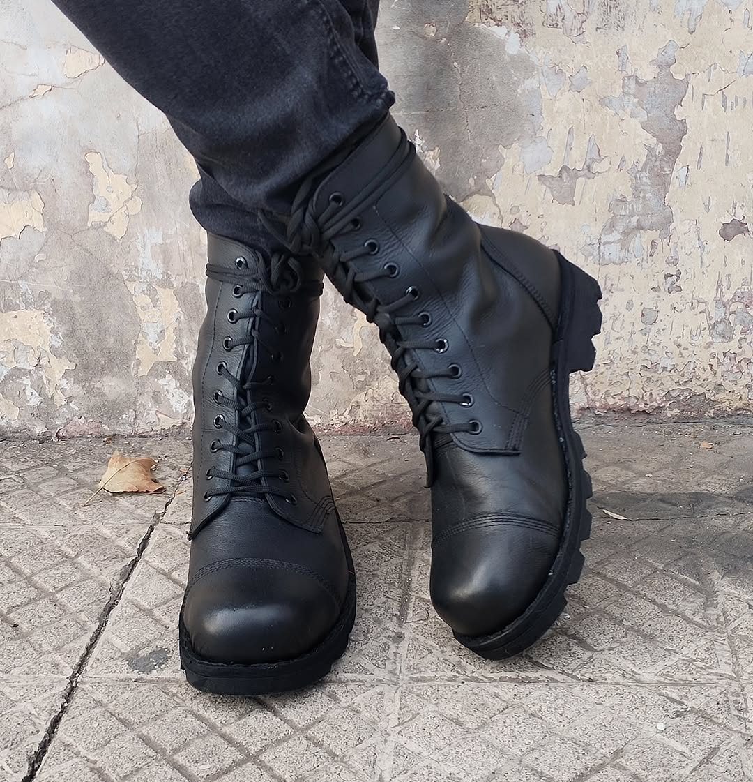 Black leather lace-up combat boots worn with dark grey jeans on concrete.