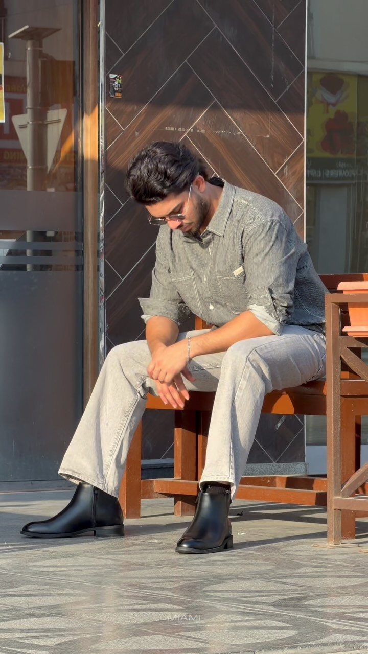 Man sitting on a bench wearing light trousers and black leather Chelsea boots.