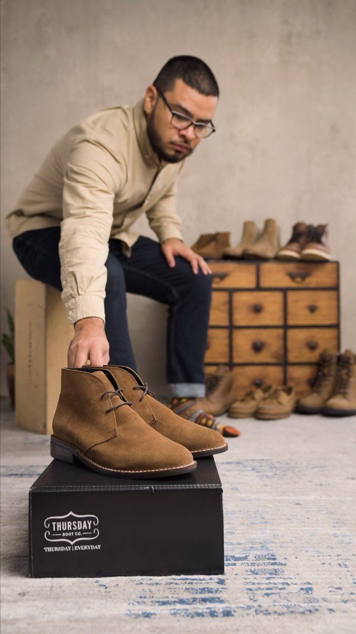 Brown suede chukka boots on a black box with a man leaning over.