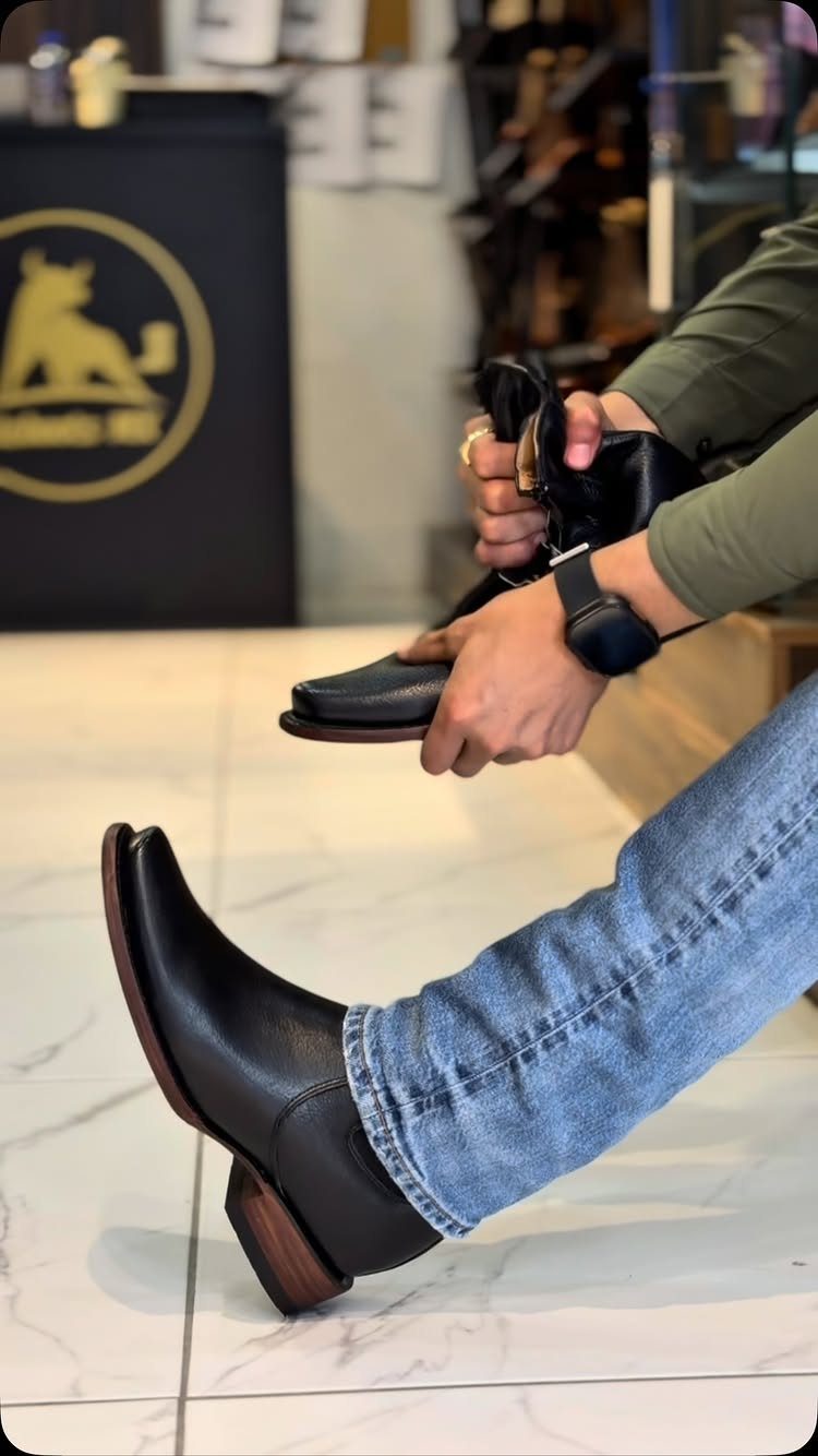 Black leather cowboy boots with pointed toes worn with blue denim jeans.