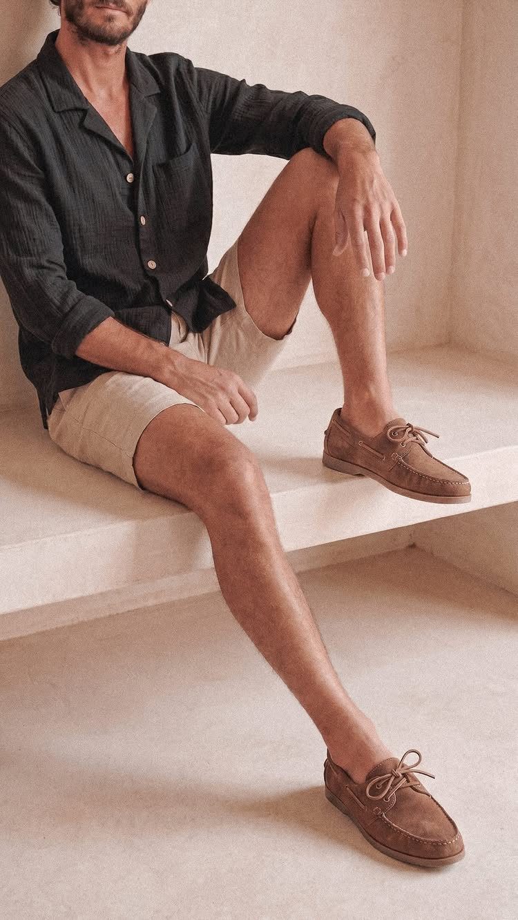 Man in beige shorts wearing brown leather boat shoes sitting on concrete ledge