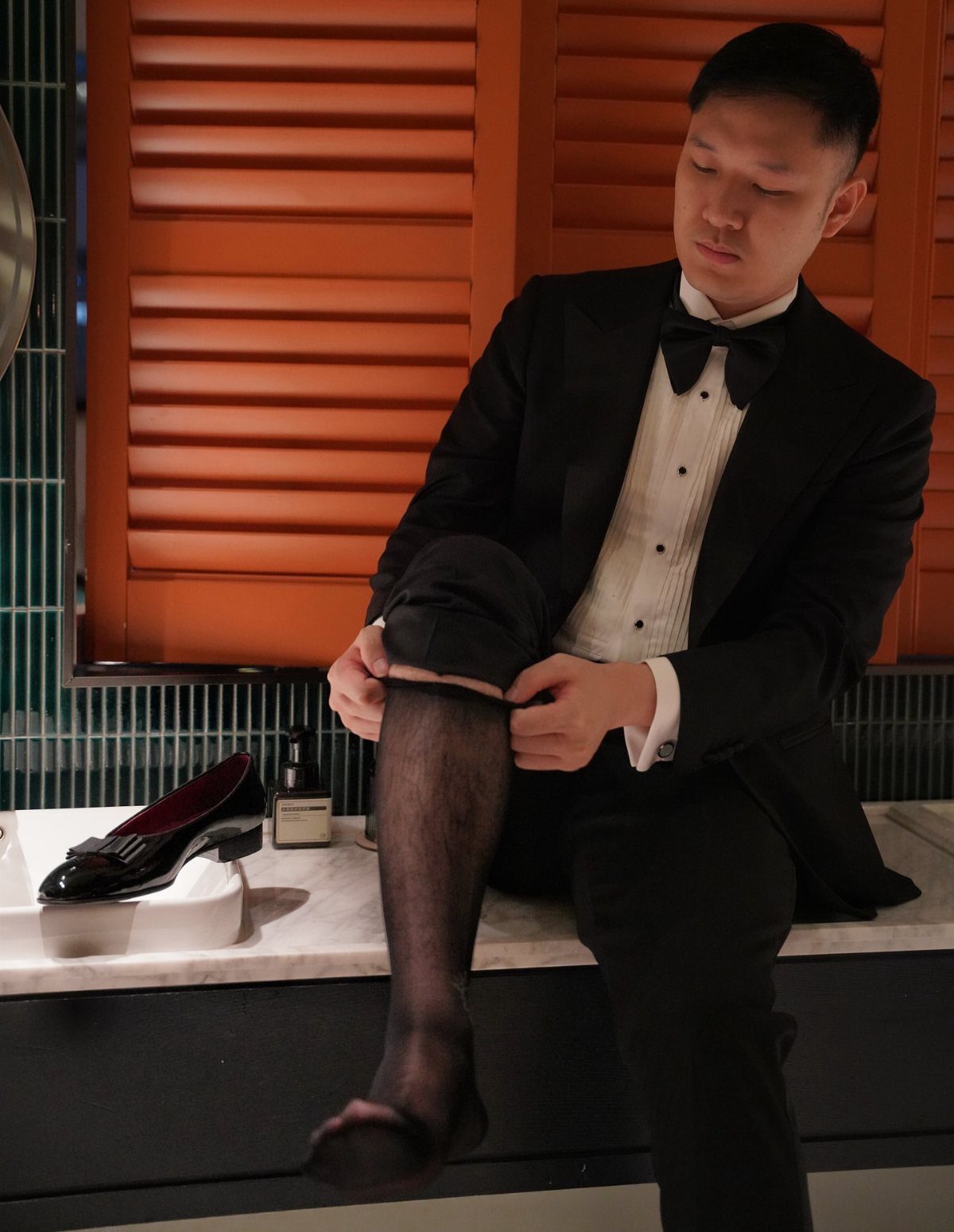 Man in tuxedo adjusting stockings next to a black patent leather opera pump shoe