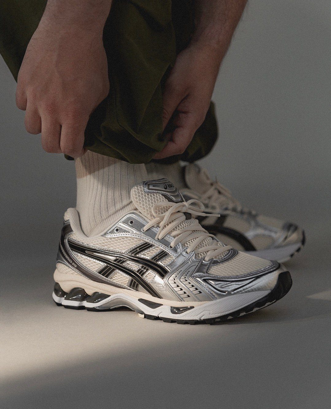 Silver and cream performance sneakers worn with olive trousers and ribbed socks.