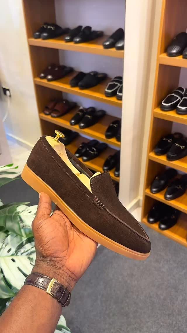 Brown suede loafer held in a hand against a backdrop of shoe shelves.