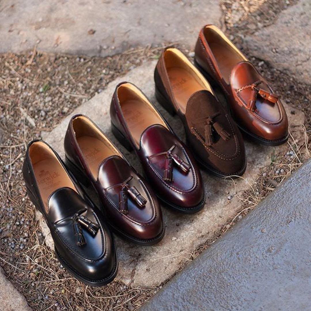 Tassel loafers in black, burgundy, and brown leather arranged on a stone ledge.