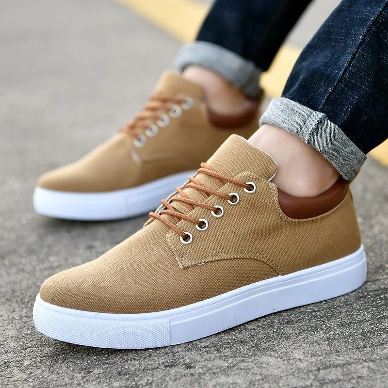 Tan canvas sneakers with white soles worn with cuffed dark blue jeans.