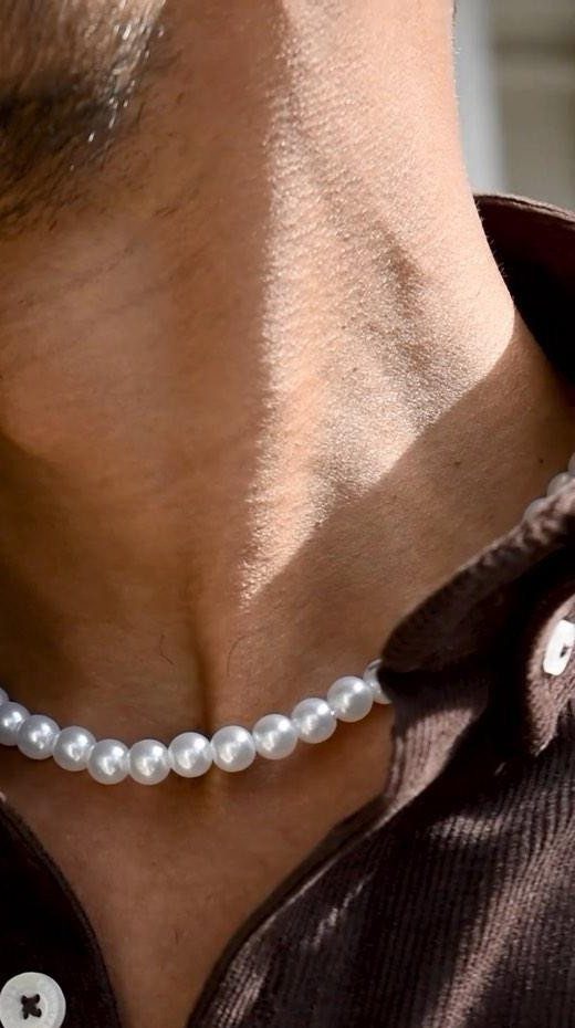 Man wearing a white pearl beaded necklace with a brown collared shirt