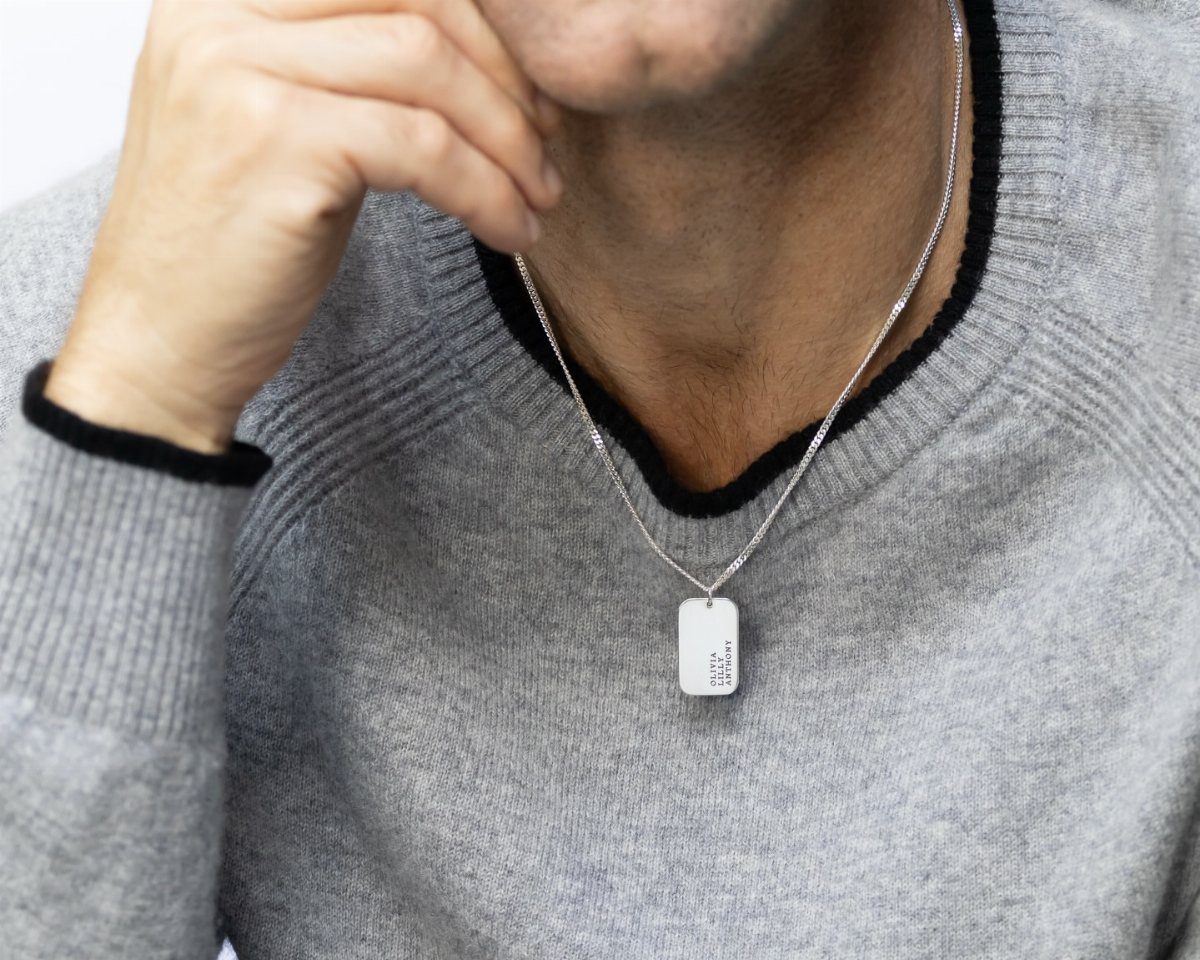 Man wearing a silver dog tag necklace over a grey knit sweater