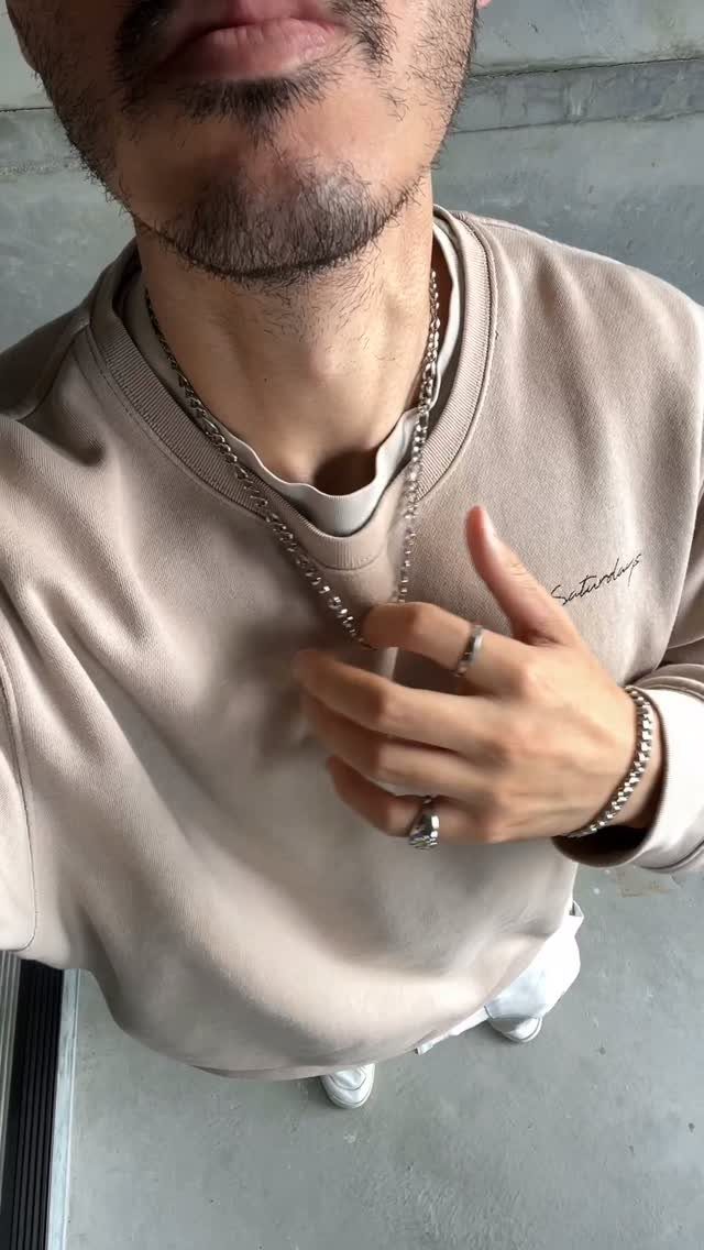 Man wearing a silver Figaro chain necklace with a beige sweatshirt and rings.