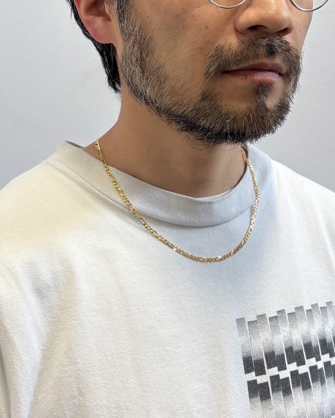 Man with a beard wearing a thin gold chain necklace and white t-shirt