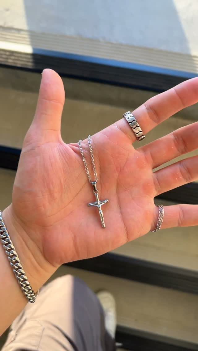 Silver cross pendant necklace resting in the palm of a man's hand.