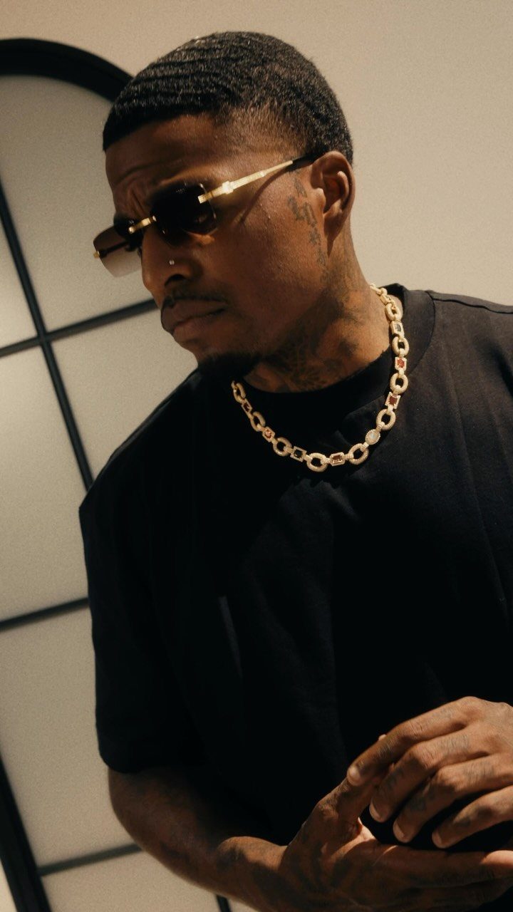 Man in black t-shirt wearing a thick gold chain necklace and sunglasses.