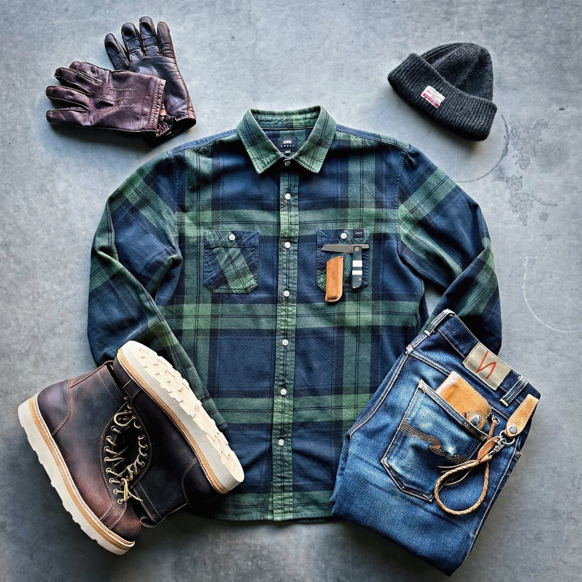 Men's rugged clothing flat lay with plaid shirt, denim jeans, and leather boots.