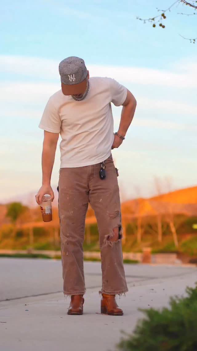 Man wearing cream shirt and brown distressed pants in a natural outdoor setting