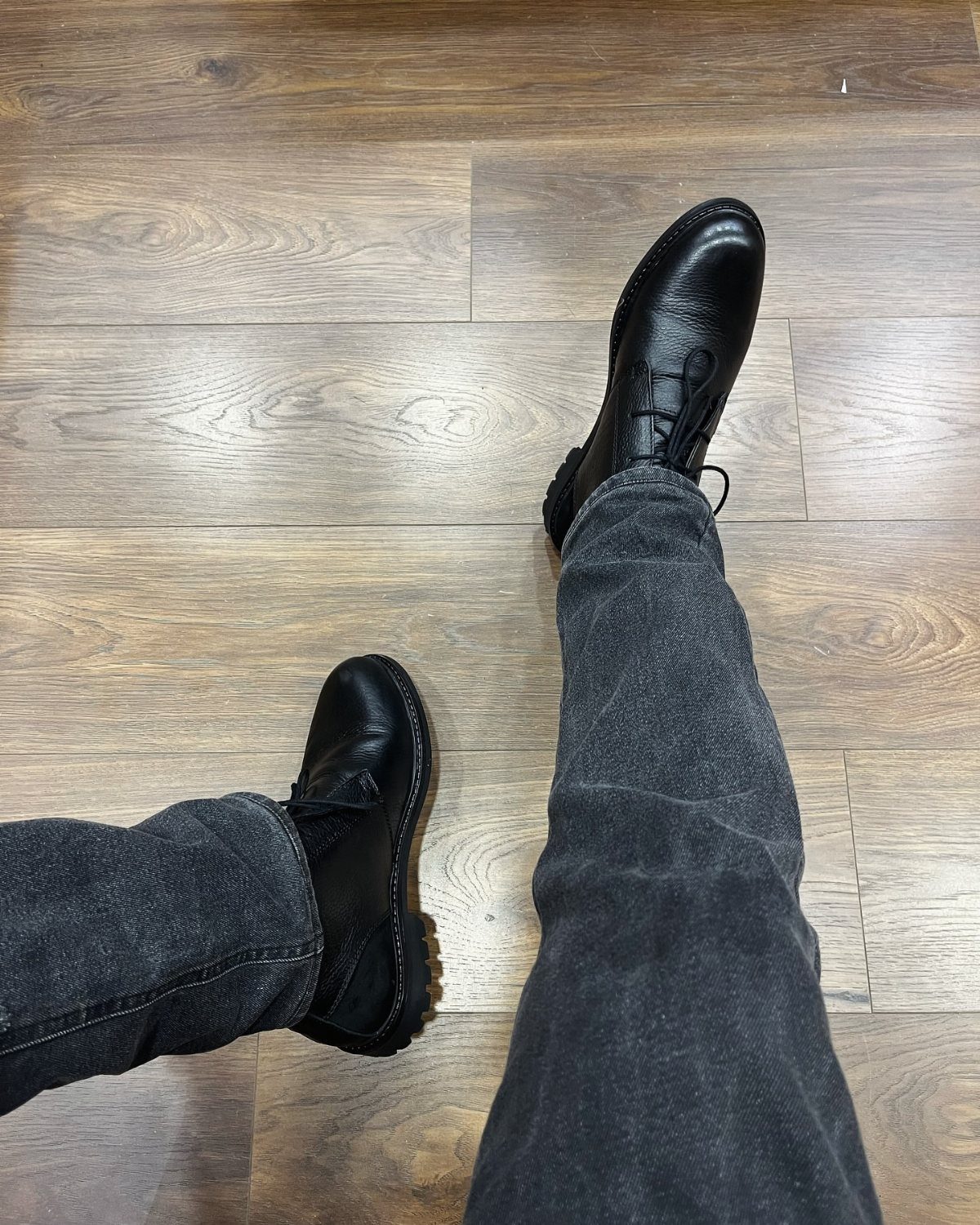 Black leather boots and dark grey jeans on a brown wooden floor