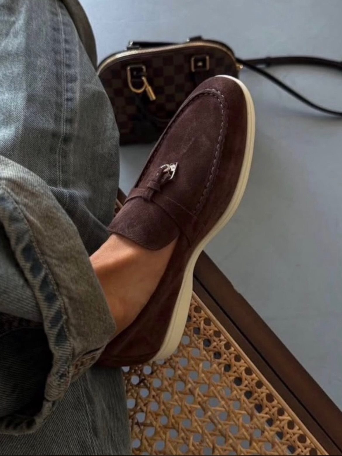 Brown suede loafers worn with cuffed grey-blue jeans and a checkered bag nearby.