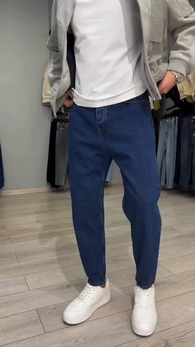 Man wearing dark blue jeans and white sneakers with a grey jacket.