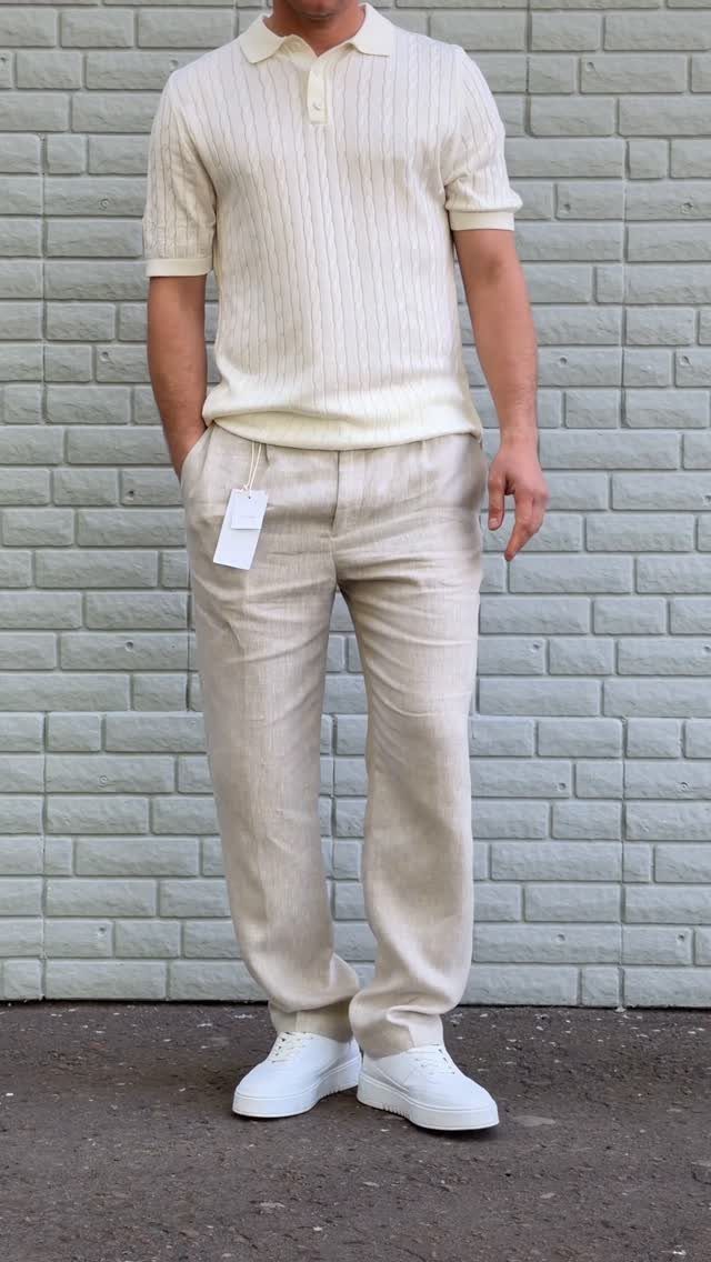Man wearing a cream polo, beige trousers, and white leather sneakers against brick wall