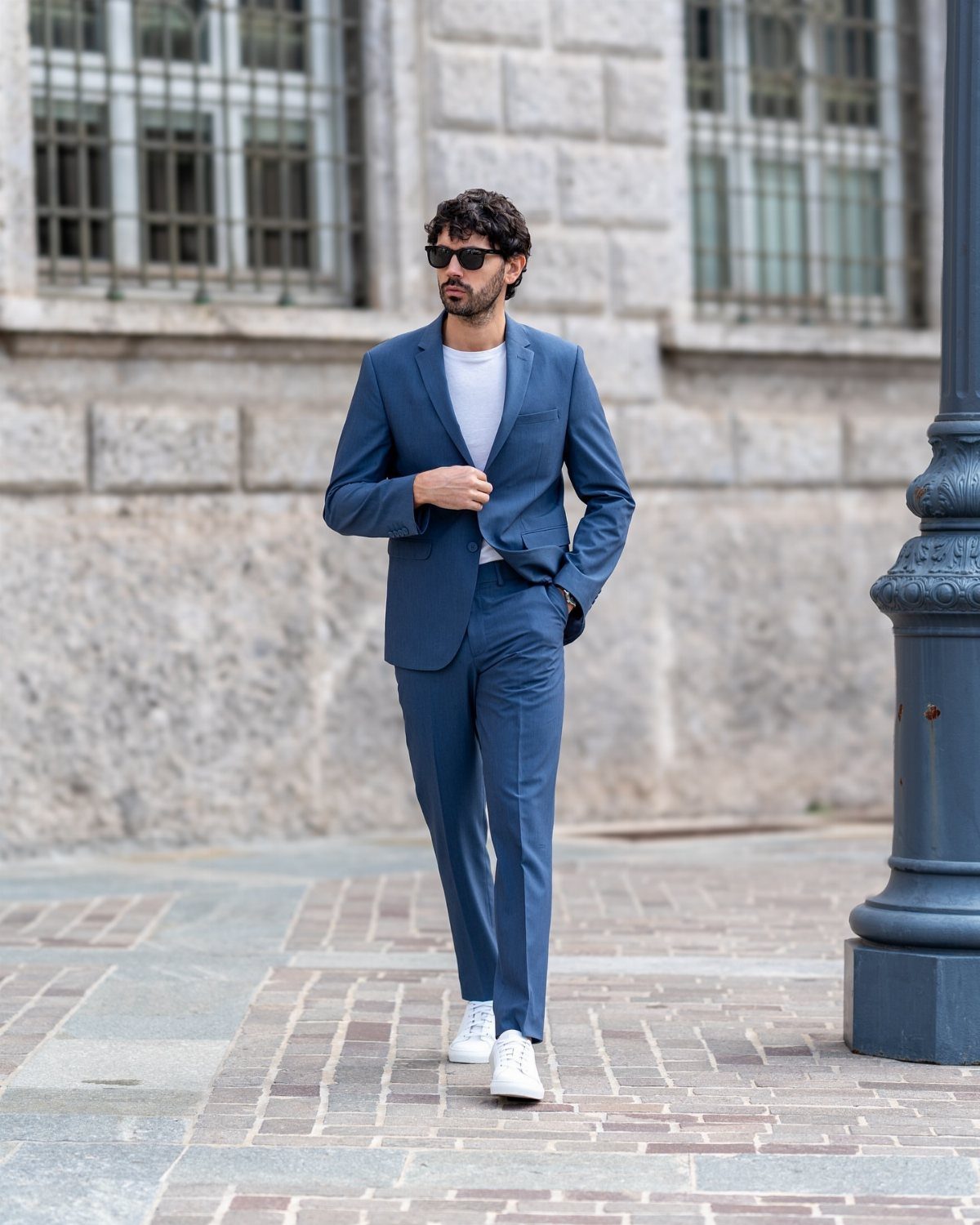 Man in a blue suit and white sneakers walking on a paved street.