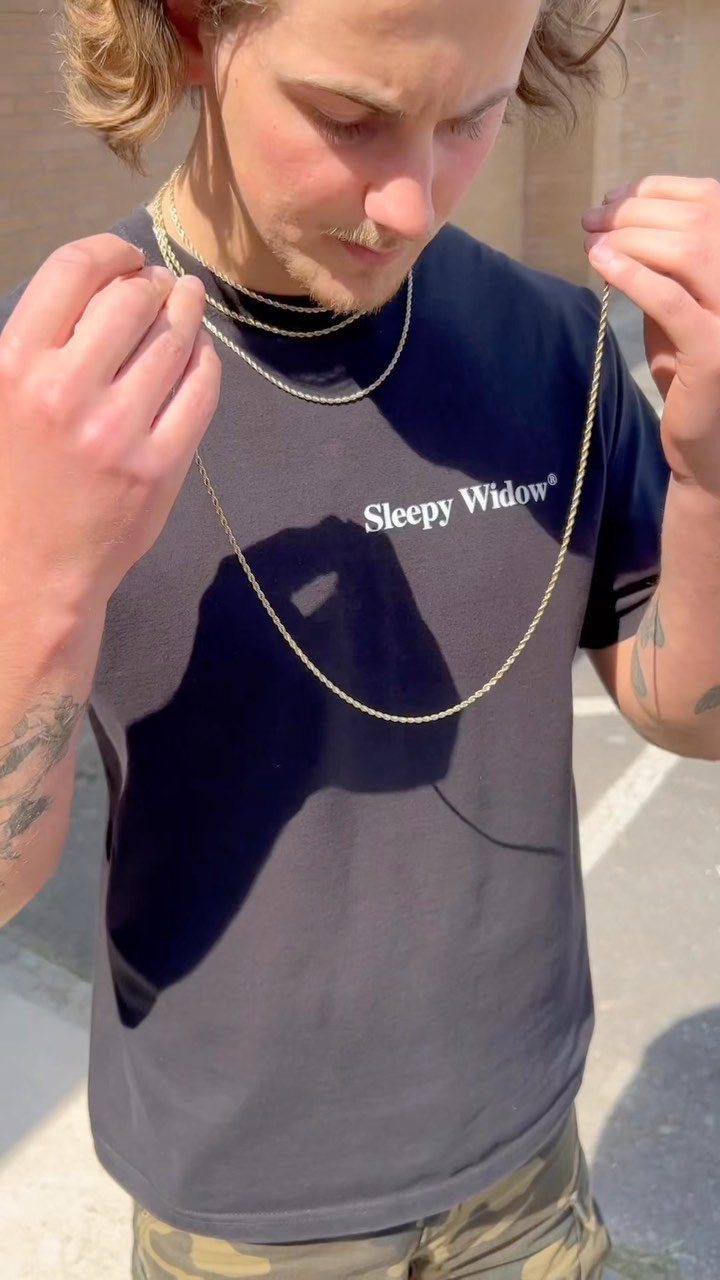Man wearing three gold necklaces of different lengths over a black t-shirt.