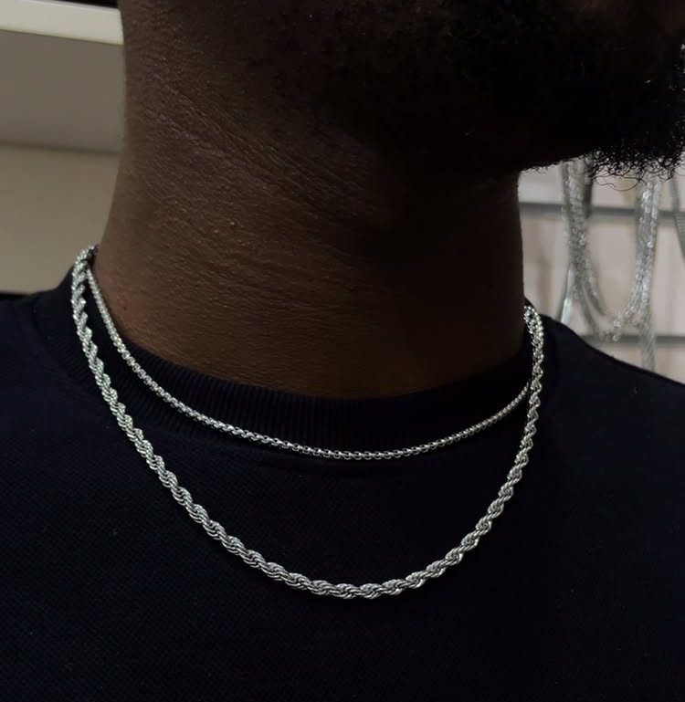 Two silver rope chain necklaces worn on a person wearing a black shirt.