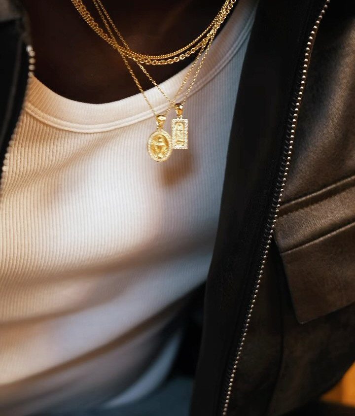Layered gold chains with an oval medallion and rectangular pendant on a person.
