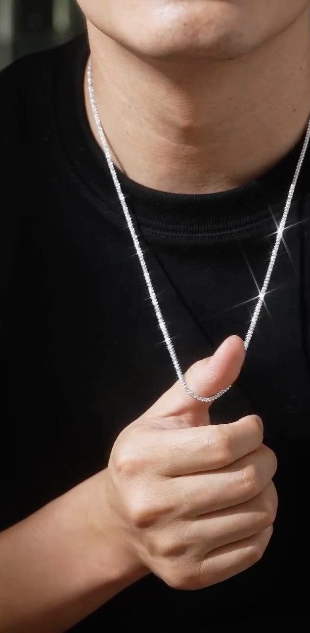 Thin silver chain necklace worn by a person in a black t-shirt