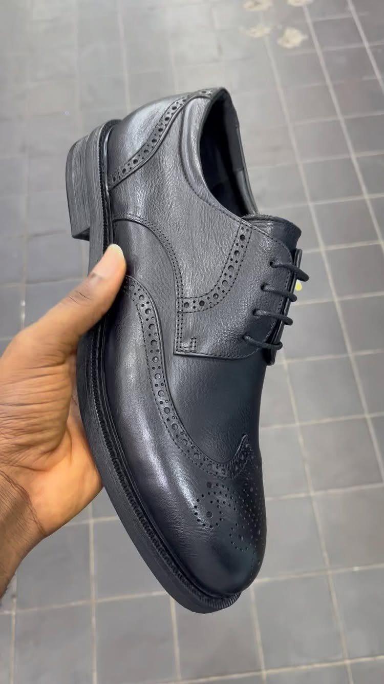 Black leather brogue shoe with decorative perforations held by a person's hand.