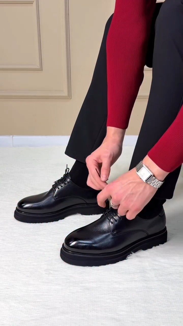 Black leather derby shoes with thick soles being tied by a man.