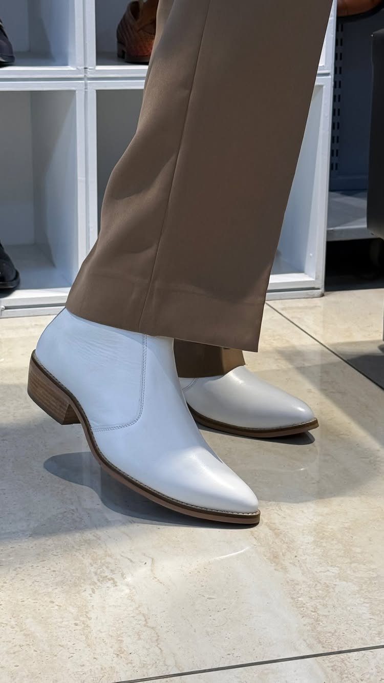 White leather ankle boots worn with tan trousers on a tiled floor