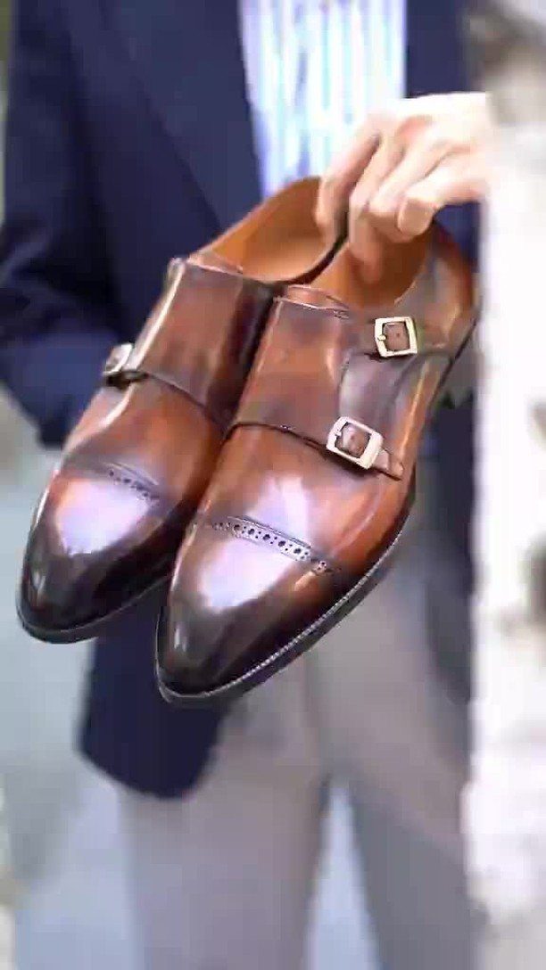 Brown leather double monk strap shoes held by a person in a blazer.