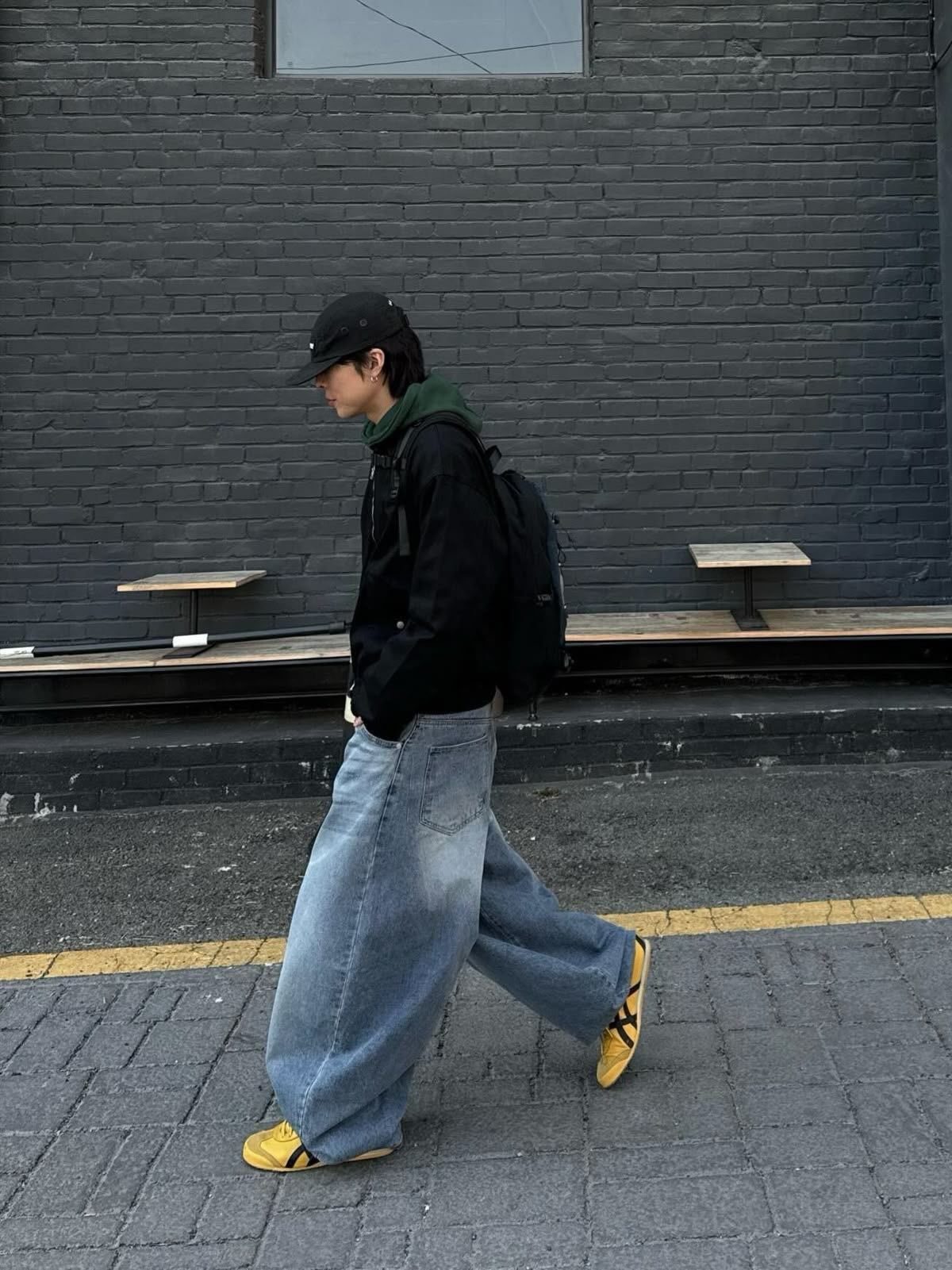 Person in black hoodie and wide-leg denim jeans wearing yellow Onitsuka Tiger sneakers.